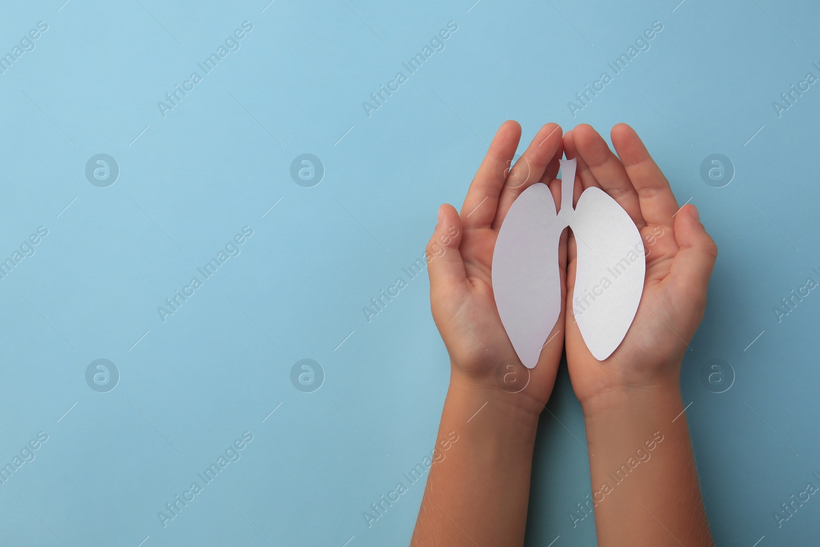 Photo of Child holding paper human lungs on light blue background, top view. Space for text