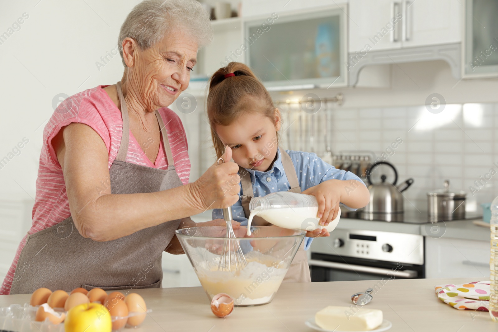 Photo of Cute girl and her grandmother cooking in kitchen