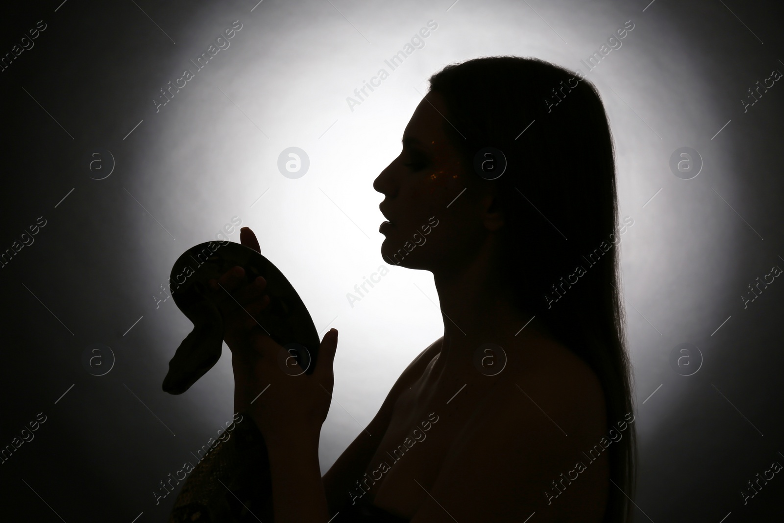 Photo of Silhouette of woman with boa constrictor on dark background