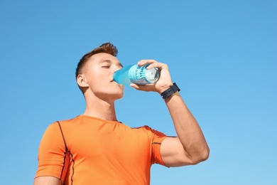 Photo of Young sporty man drinking water from bottle against blue sky on sunny day