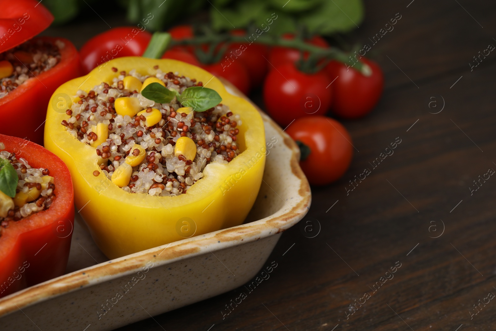 Photo of Quinoa stuffed bell peppers and basil in baking dish on wooden table, closeup. Space for text