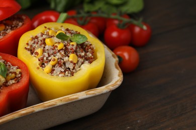 Photo of Quinoa stuffed bell peppers and basil in baking dish on wooden table, closeup. Space for text