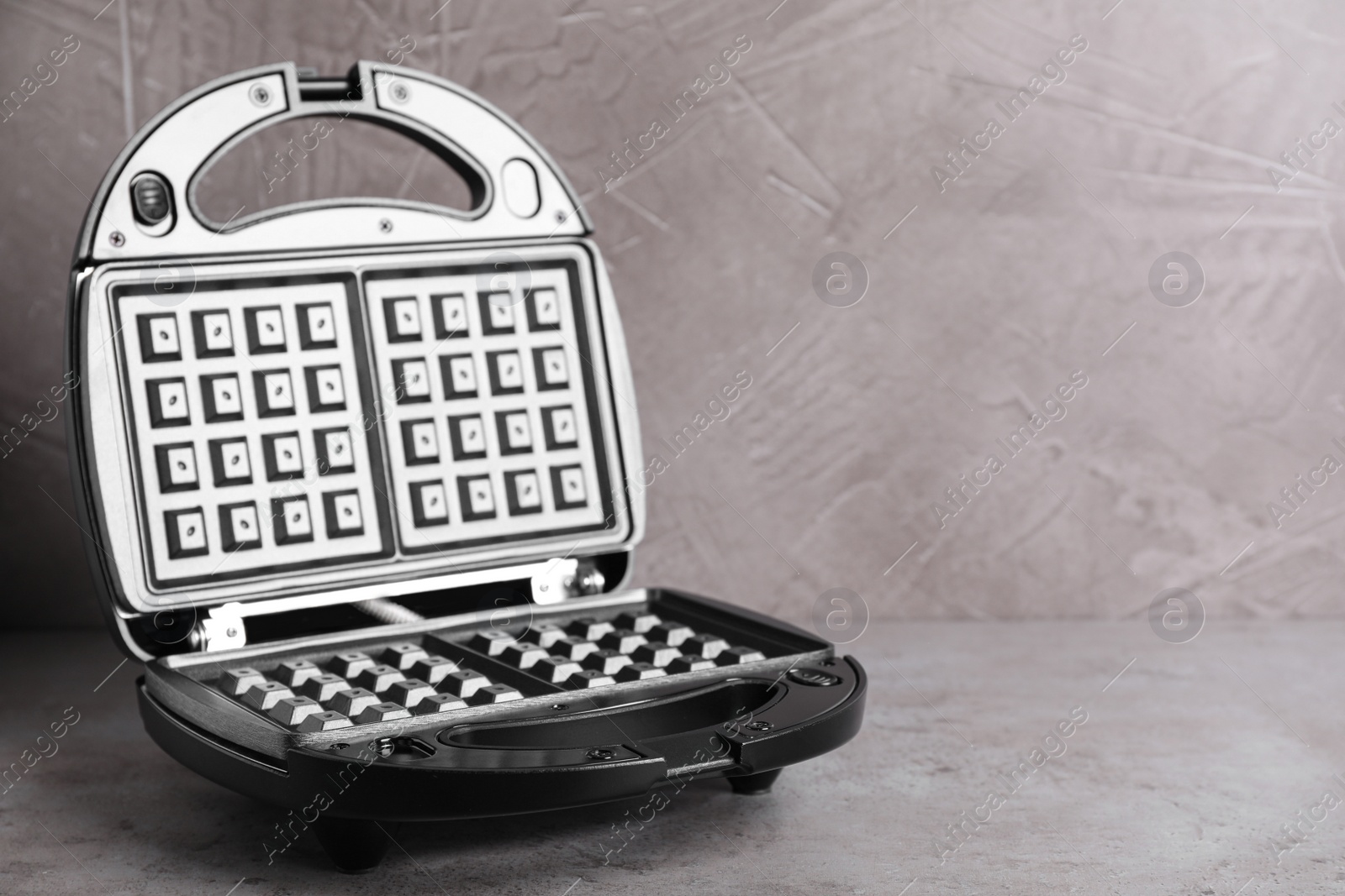 Photo of Modern waffle iron on grey stone table. Space for text