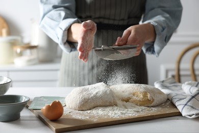 Photo of Making dough. Woman sifting flour at white wooden table in kitchen, closeup