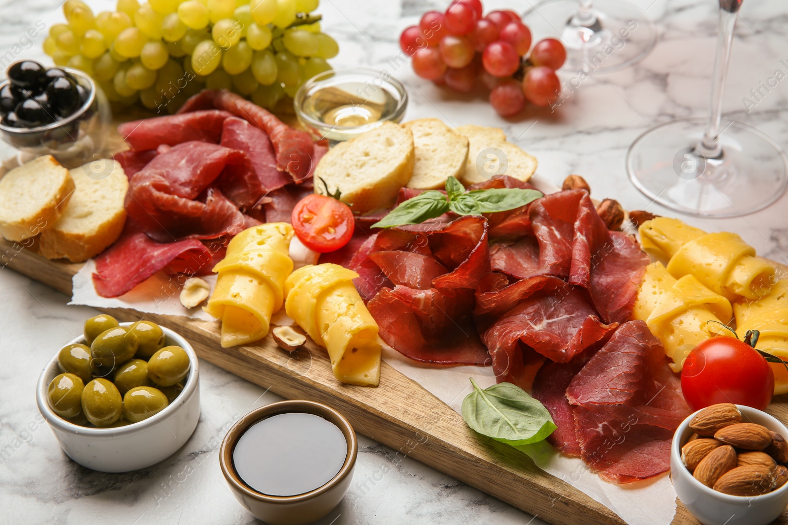 Photo of Charcuterie board. Delicious bresaola and other snacks on white marble table