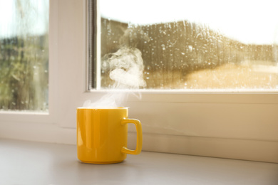 Photo of Cup of hot drink near window on rainy day. Space for text