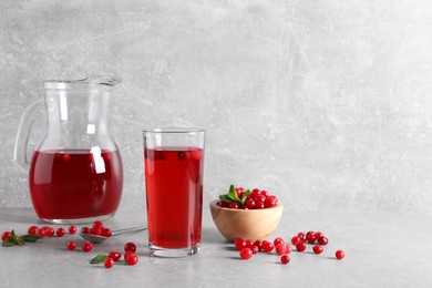 Photo of Tasty cranberry juice in glass and fresh berries on light grey table