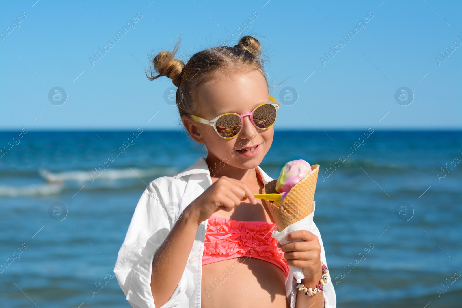 Photo of Adorable little girl with delicious ice cream near sea on sunny summer day