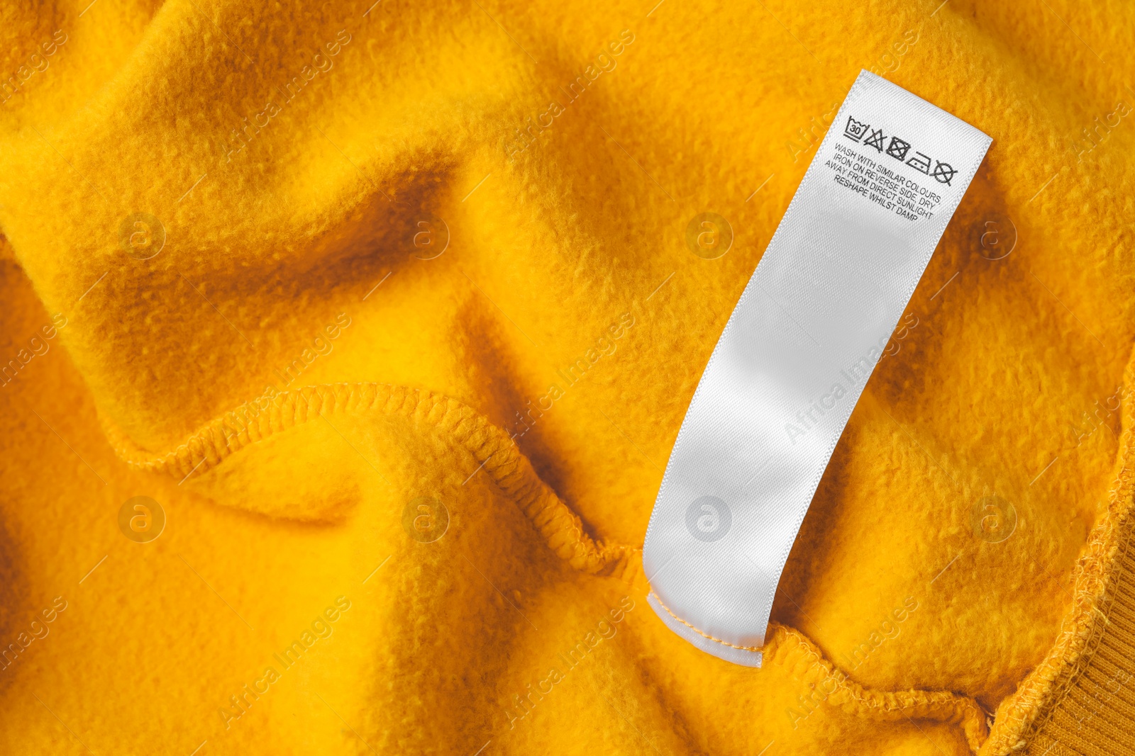 Photo of Clothing label with care recommendations on orange garment, top view. Space for text