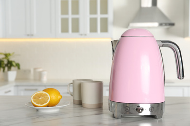 Photo of Modern electric kettle, cups and lemons on table in kitchen