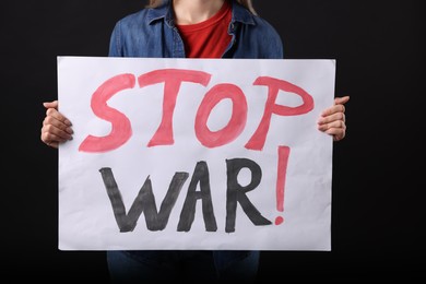 Photo of Woman holding poster with words Stop War on black background, closeup