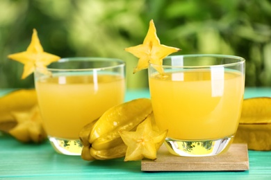 Photo of Delicious carambola juice and fresh fruits on light blue wooden table against blurred background