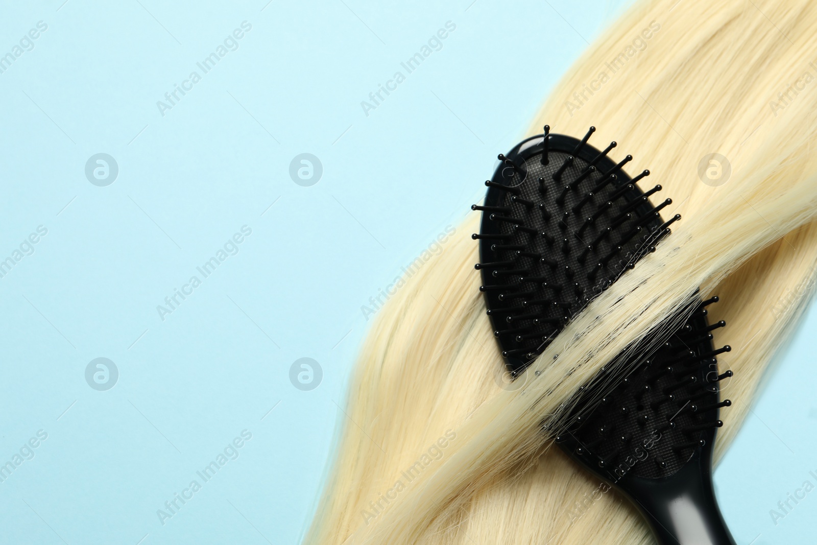 Photo of Stylish brush with blonde hair strand on light blue background, top view. Space for text