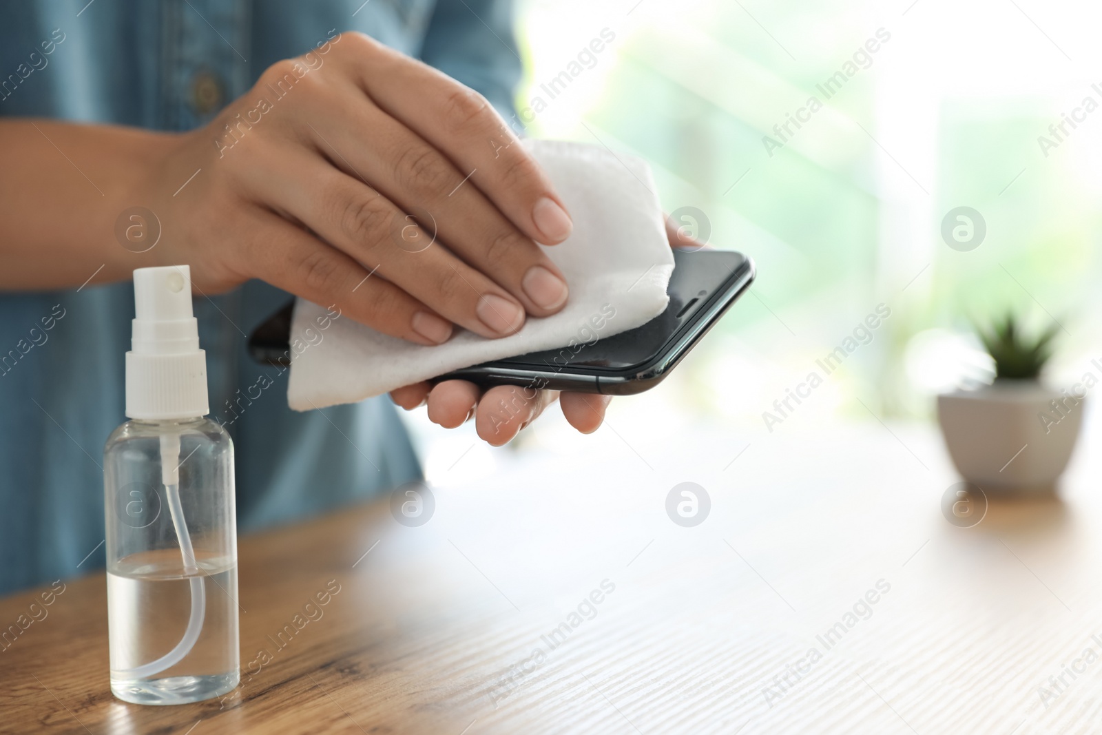 Photo of Woman cleaning smartphone with wet wipe at wooden table, closeup