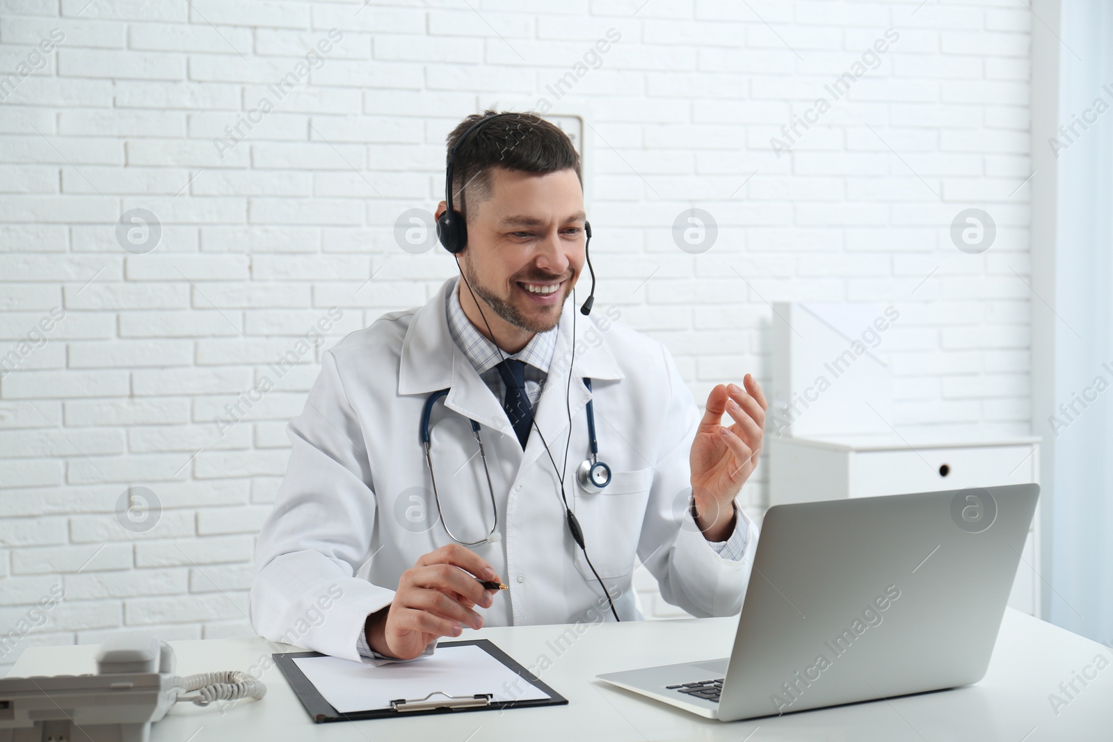 Photo of Doctor with headset consulting patient online at desk in clinic. Health service hotline