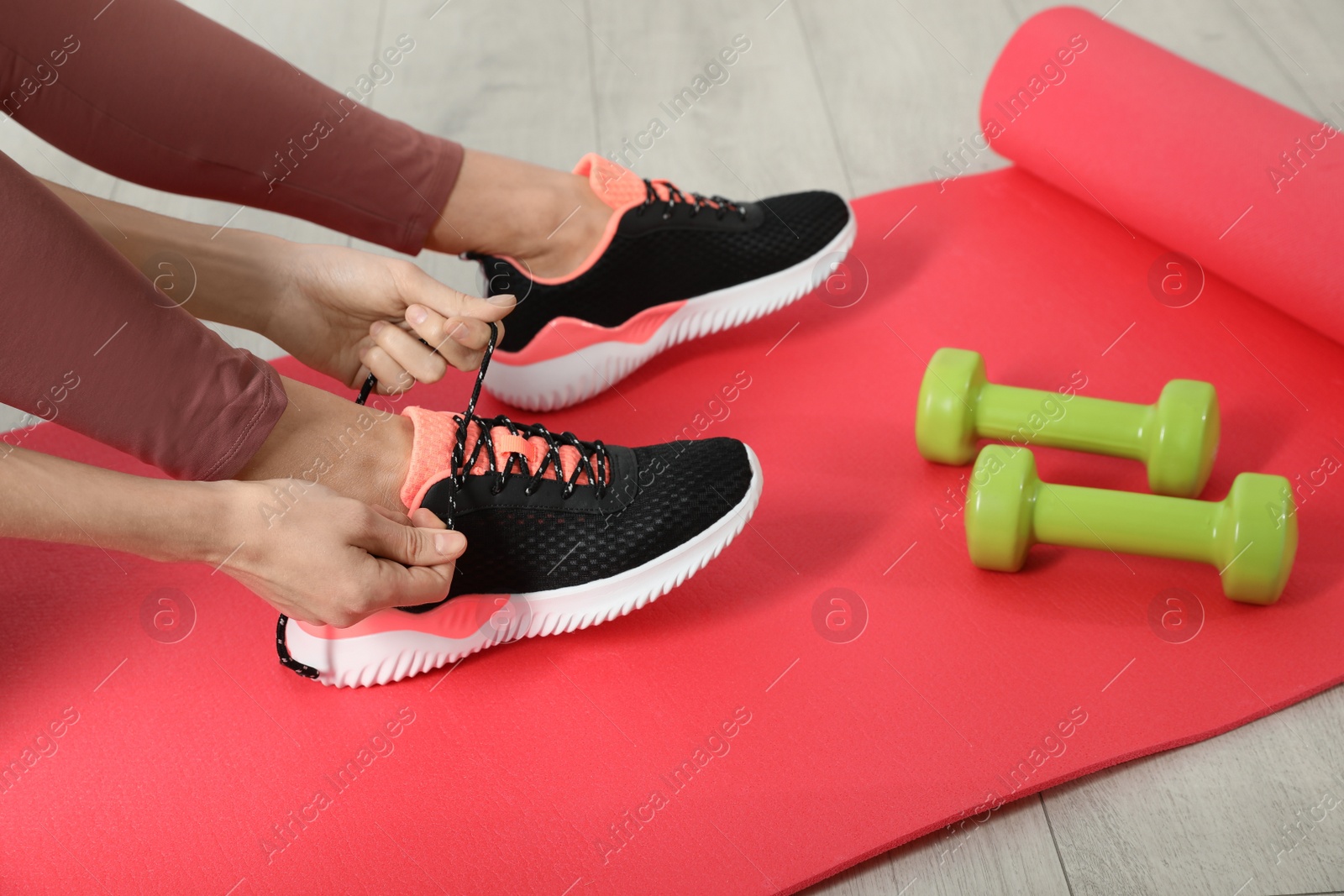 Photo of Woman tying sneaker's shoelaces on exercise mat, closeup