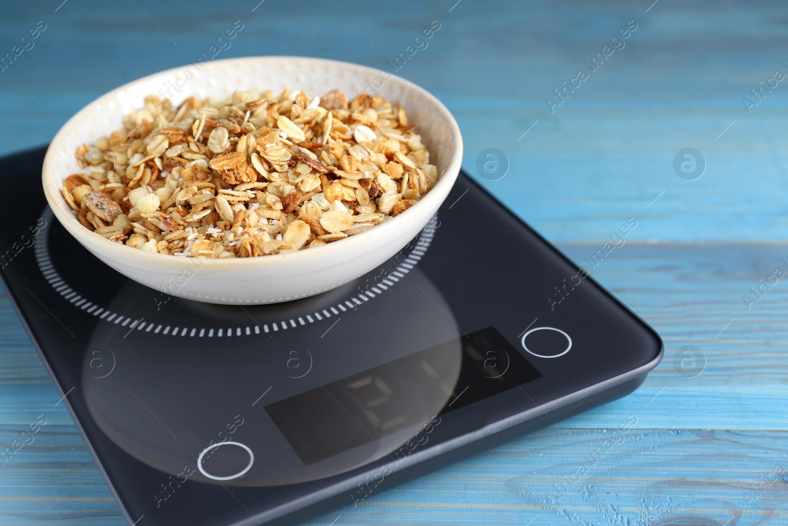 Photo of Electronic scales with granola on light blue wooden table, closeup