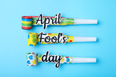Photo of Party horns with words APRIL FOOL'S DAY on light blue background, flat lay