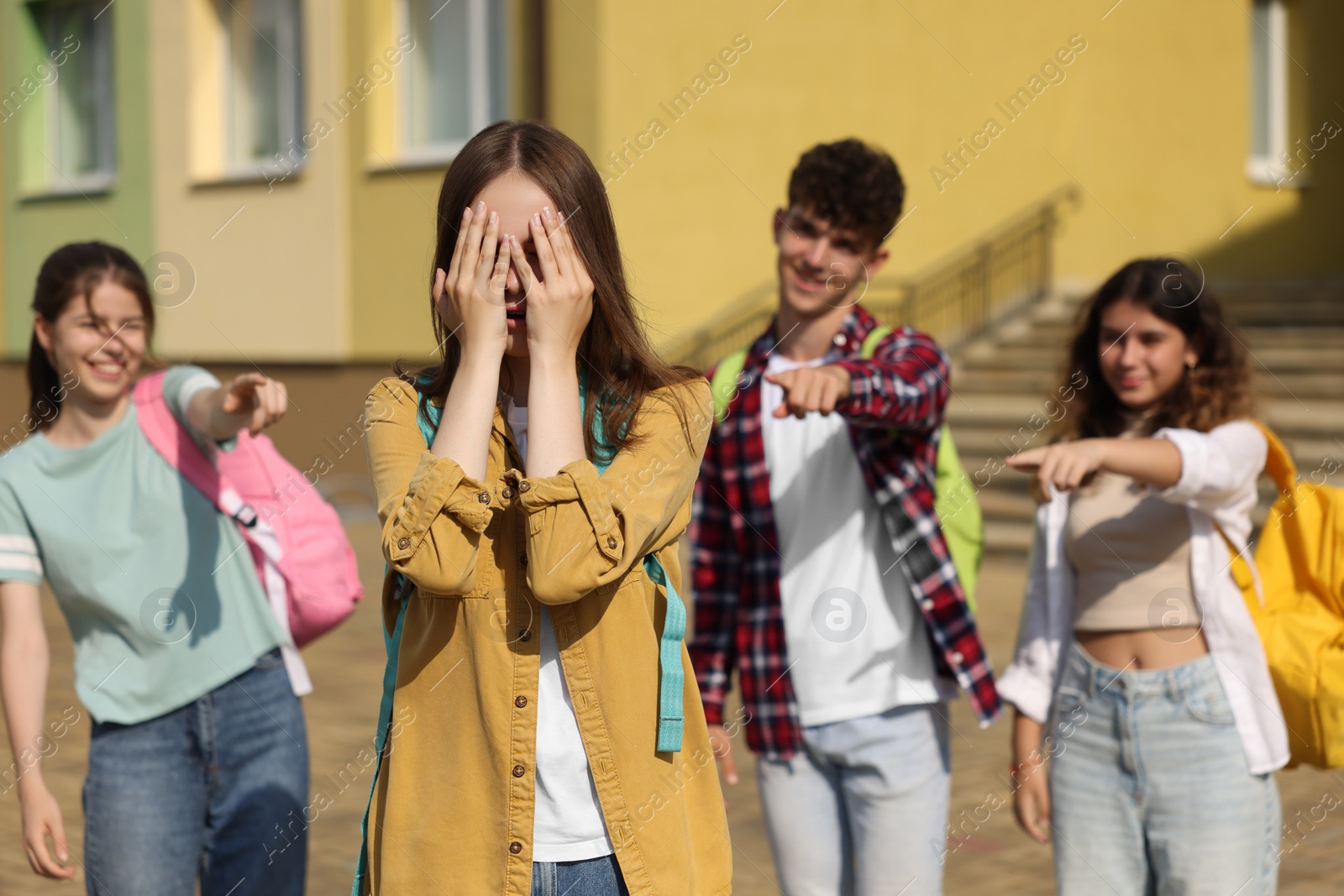 Photo of Teen problems. Group of students pointing at upset girl outdoors, selective focus