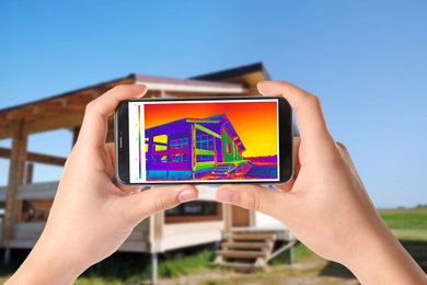 Image of Woman detecting heat loss in house using thermal viewer on smartphone, outdoors. Energy efficiency