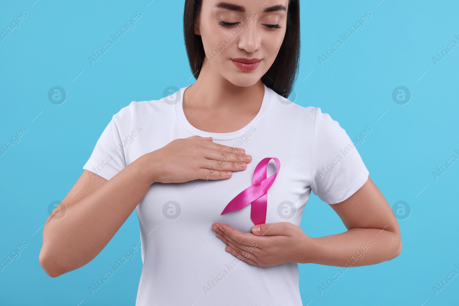 Photo of Beautiful woman with pink ribbon on light blue background. Breast cancer awareness