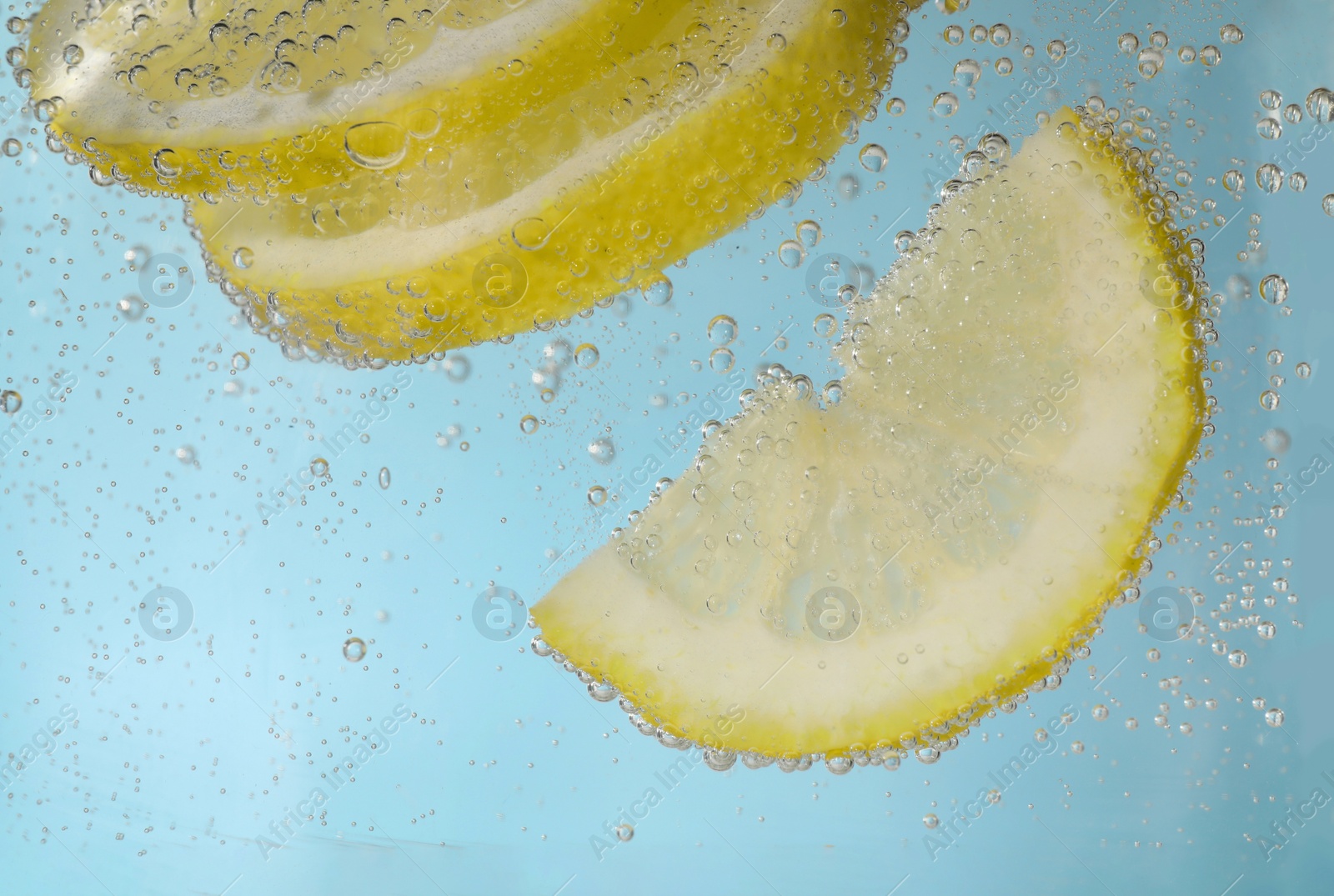 Photo of Juicy lemon slices in soda water against light blue background, closeup