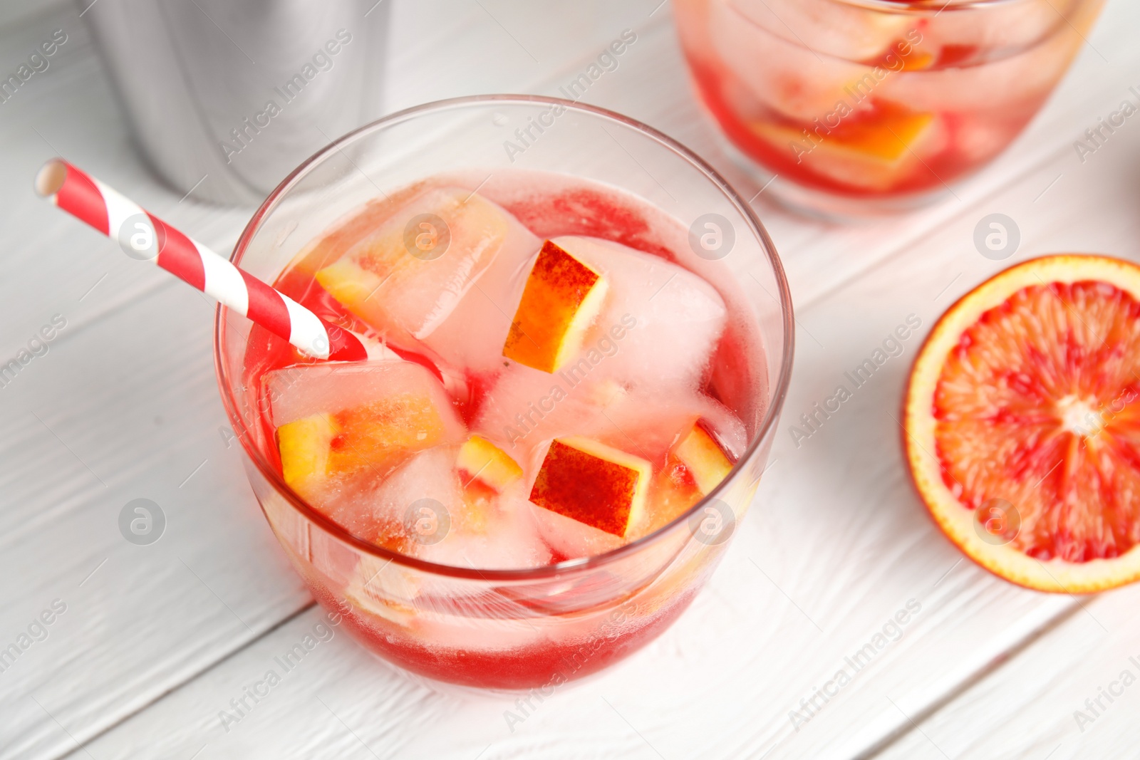 Photo of Glass of tropical cocktail with ice cubes and fruit on white table