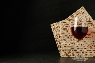 Photo of Passover matzos and glass of wine on black background, space for text. Pesach celebration
