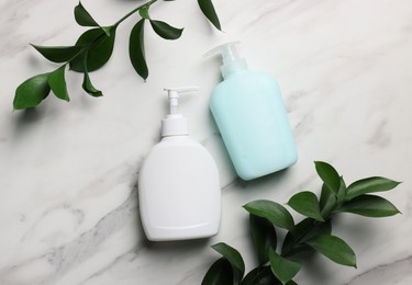 Dispensers of liquid soap and branches on white marble table, flat lay