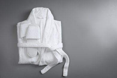 Photo of Clean folded bathrobe and slippers on grey background, top view. Space for text