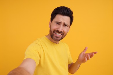 Emotional man taking selfie on yellow background