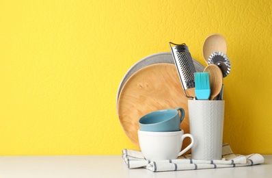 Different kitchen utensils on white table against yellow background. Space for text