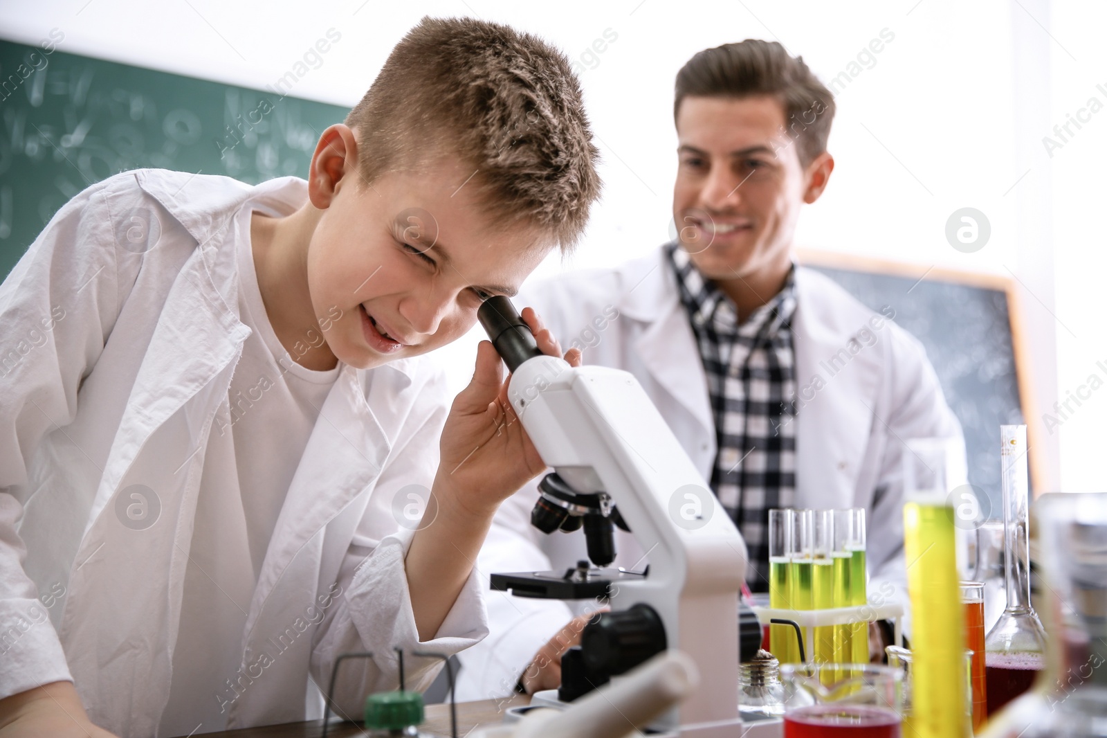 Photo of Teacher with pupil using microscope in chemistry class