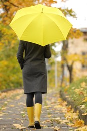Photo of Woman with yellow umbrella walking in autumn park, back view