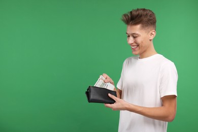 Photo of Happy man putting money into his wallet on green background. Space for text