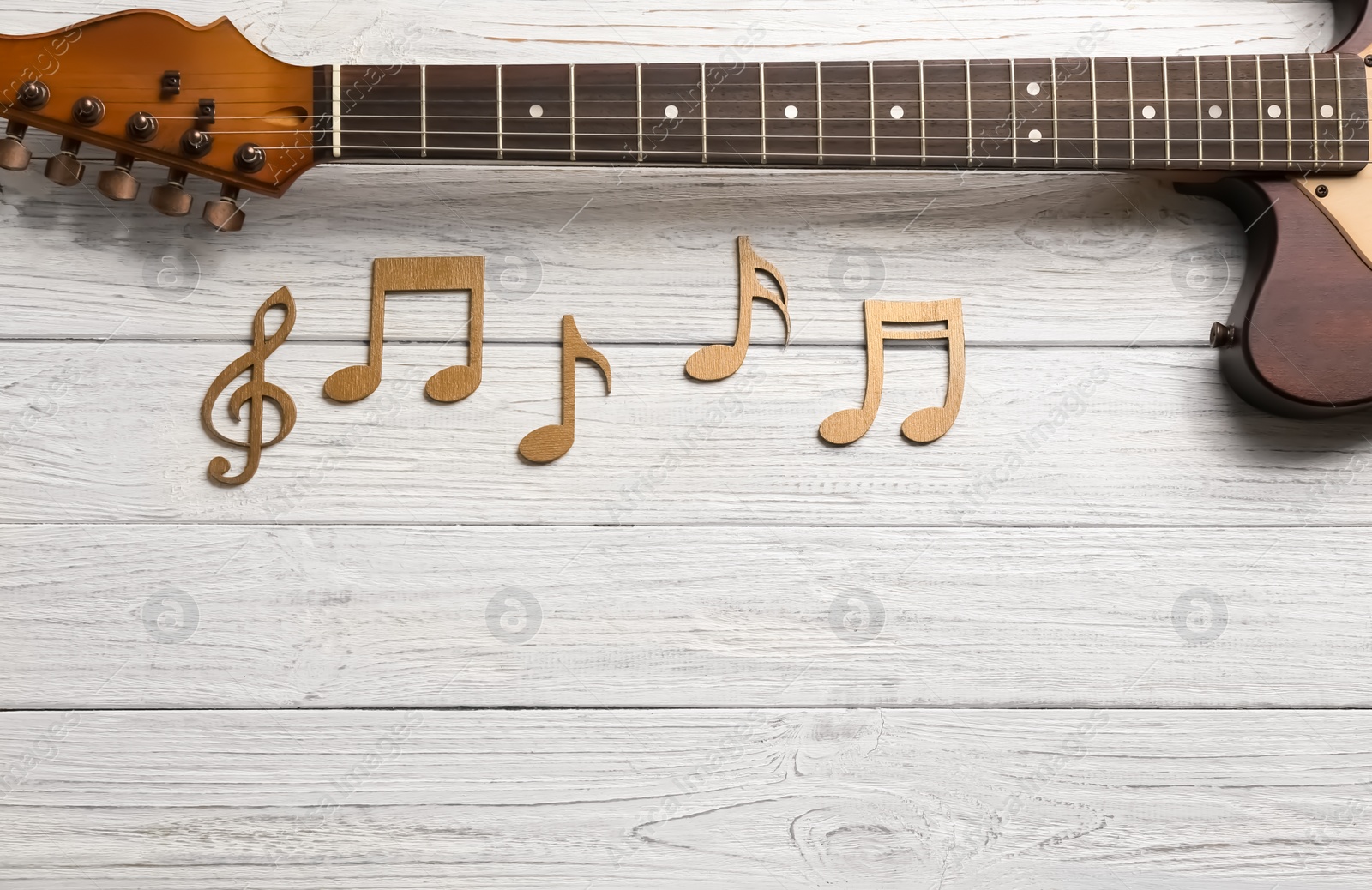 Photo of Music notes and guitar neck on wooden background, top view. Space for text