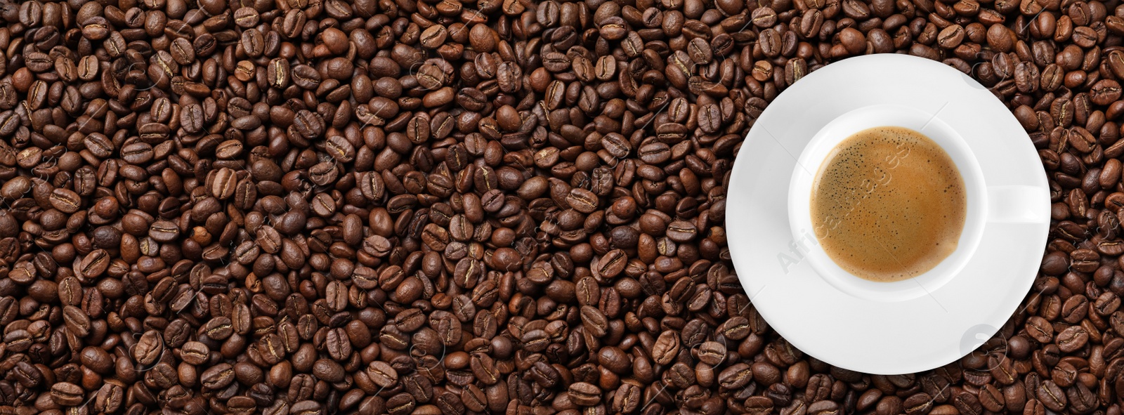 Image of Cup of tasty aromatic coffee on roasted beans, top view. Banner design