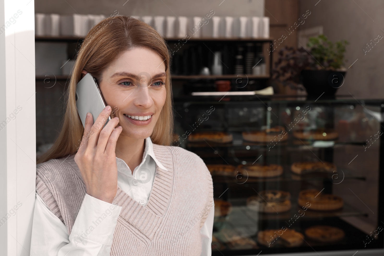 Photo of Happy business owner talking on phone in bakery shop. Space for text