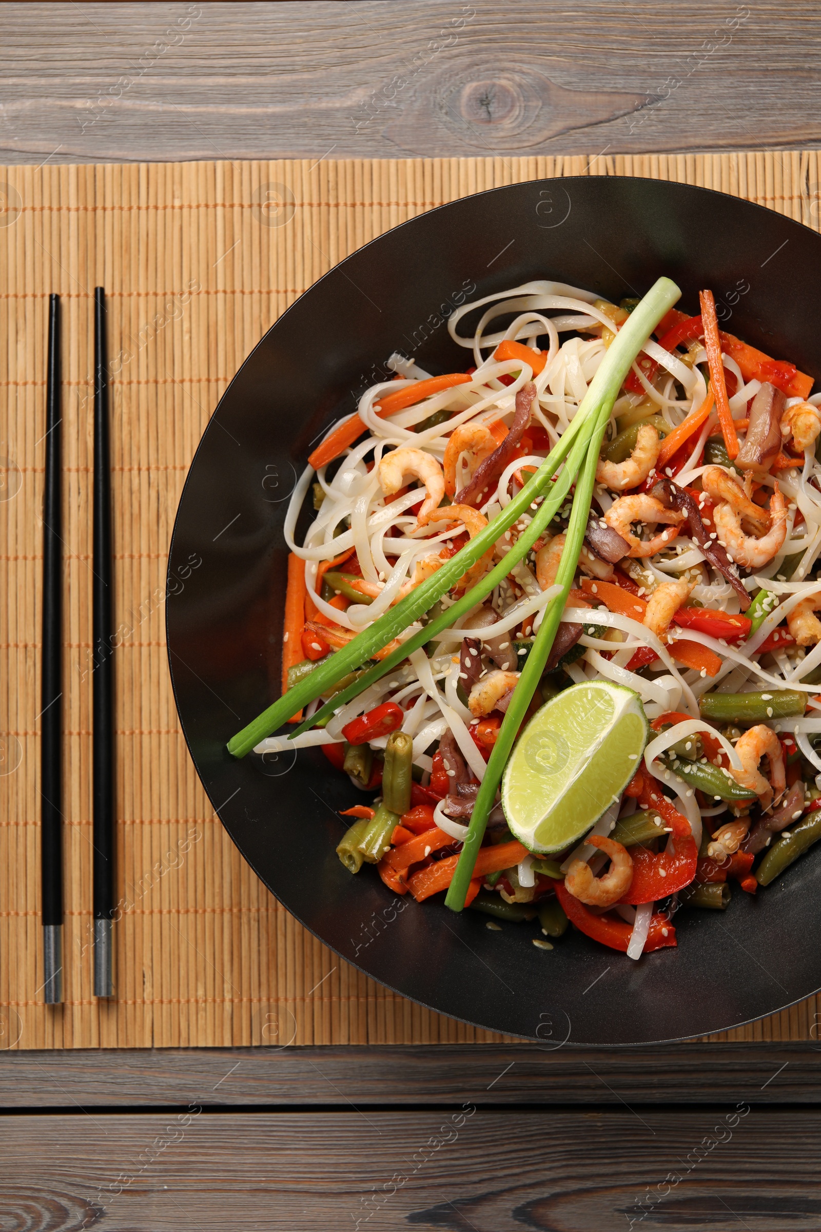 Photo of Shrimp stir fry with noodles and vegetables in wok on wooden table, top view