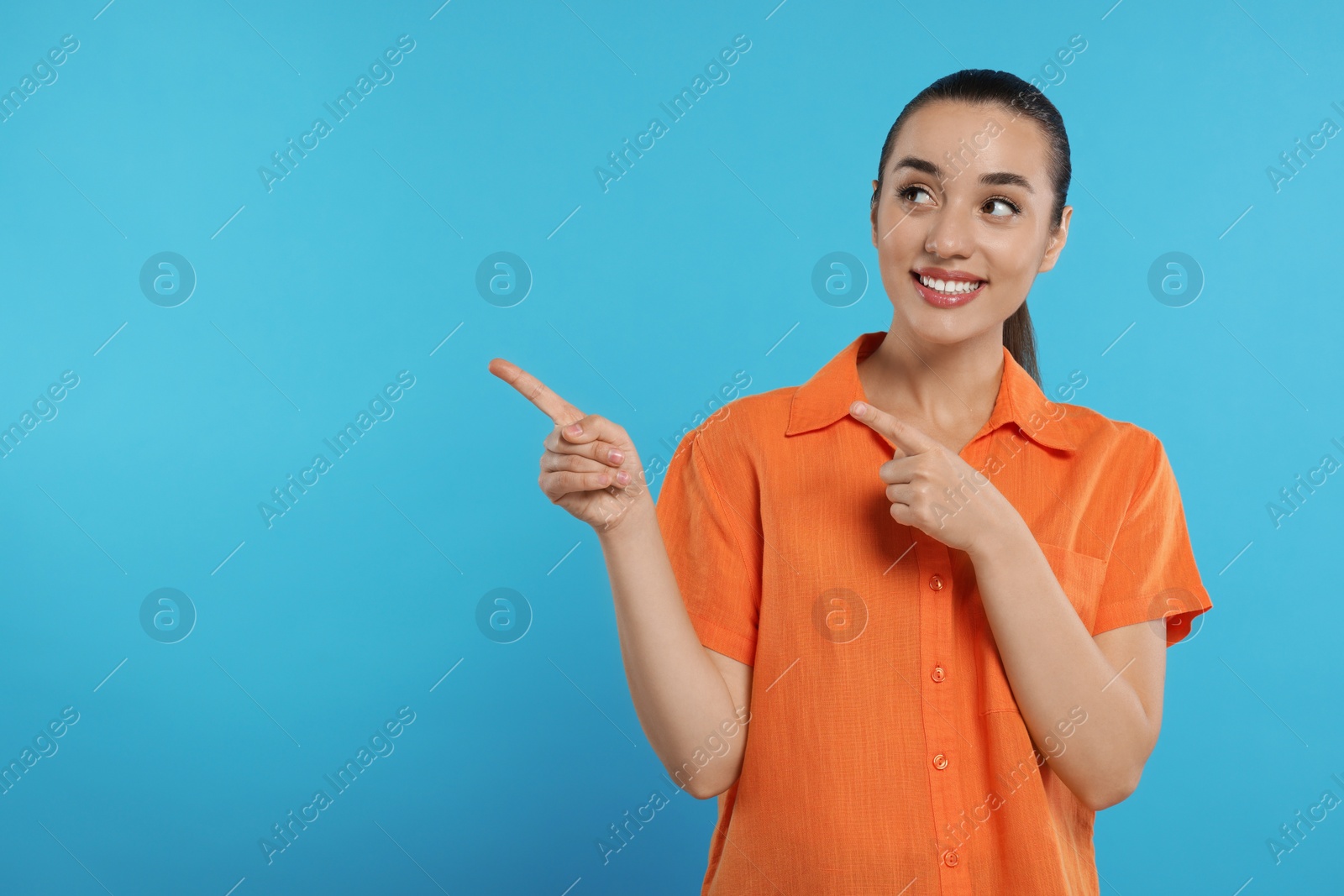 Photo of Special promotion. Smiling woman pointing at something on light blue background. Space for text
