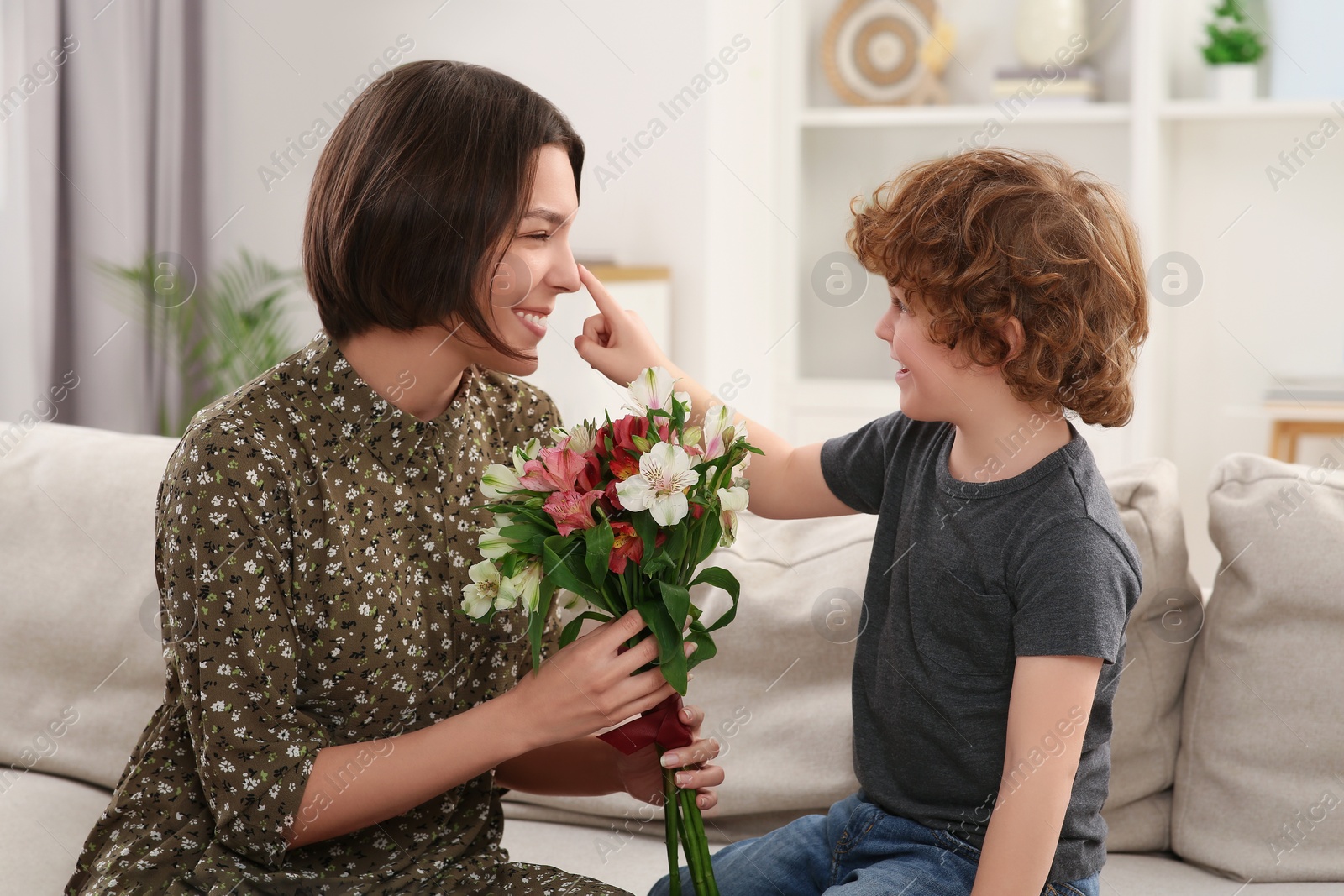 Photo of Little son congratulating his mom with Mother`s day at home. Woman holding bouquet of flowers