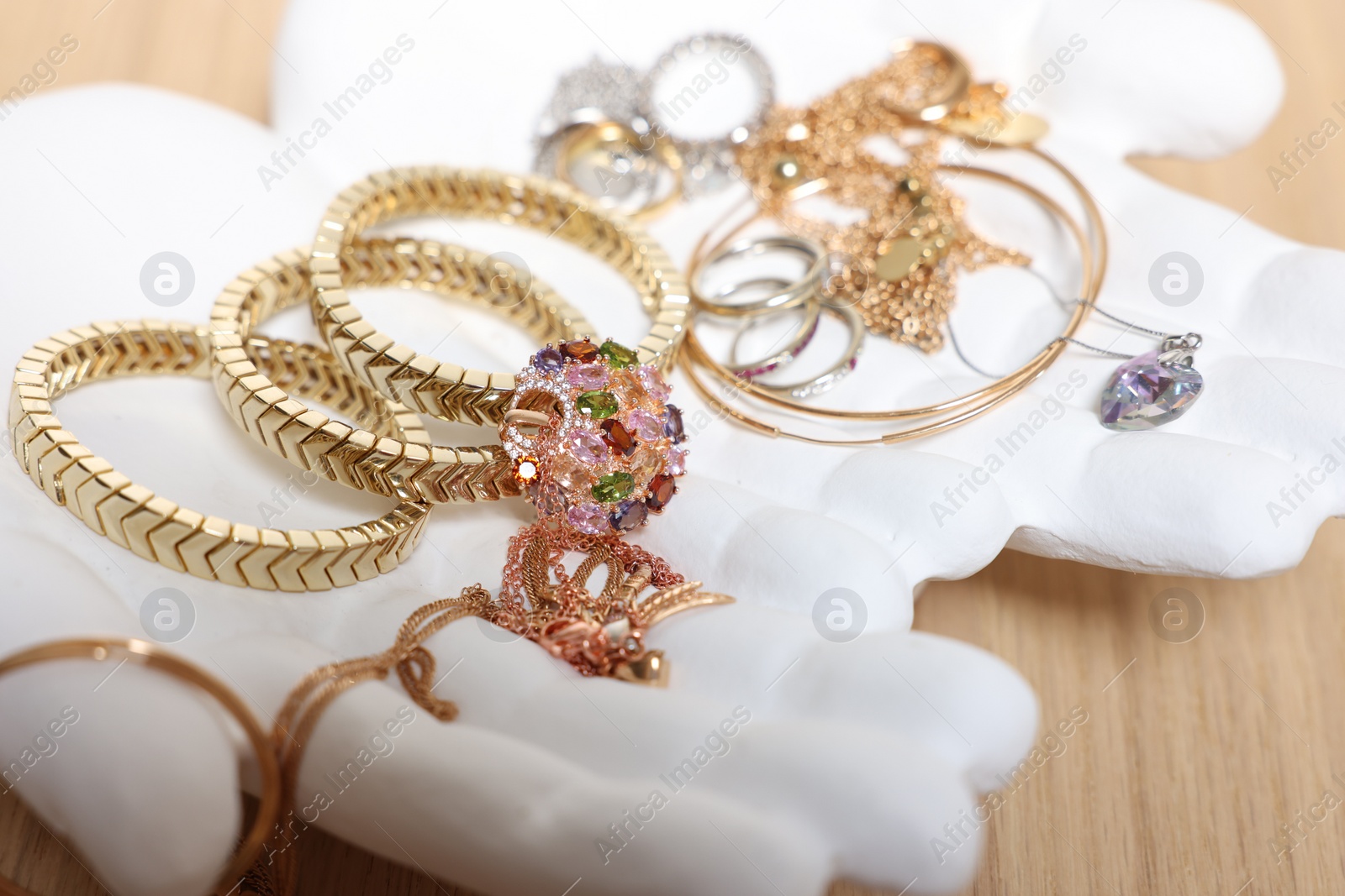 Photo of Ceramic hand stand with stylish bracelets and other accessories on wooden table, closeup