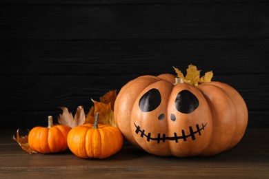 Photo of Orange pumpkins and one with drawn spooky face on wooden table. Halloween celebration