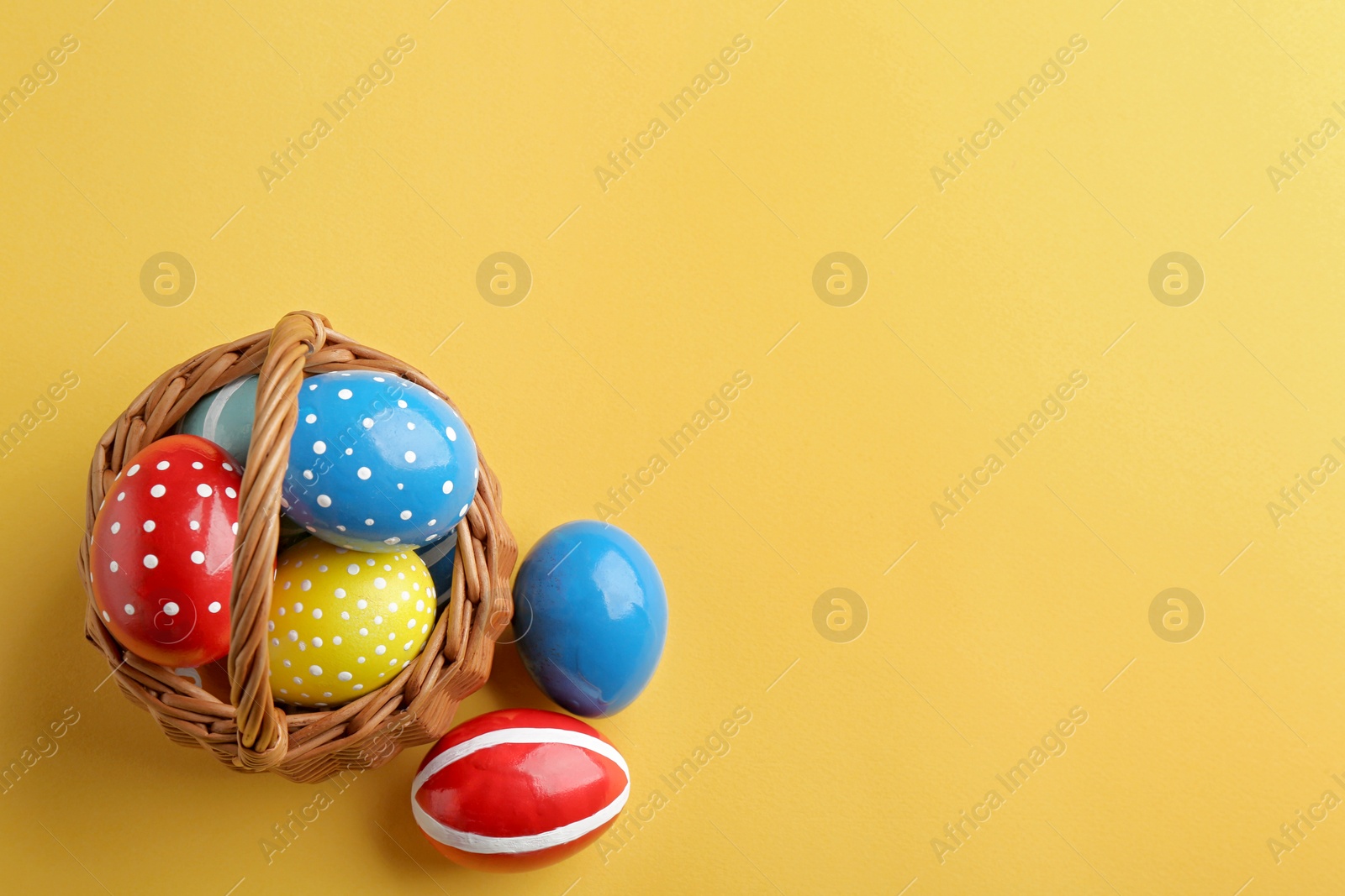 Photo of Wicker basket with painted Easter eggs on color background, top view. Space for text