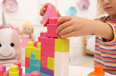 Cute little girl playing with colorful building blocks at table indoors, closeup