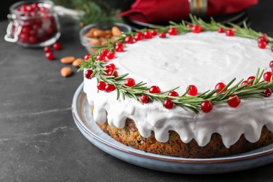 Photo of Traditional Christmas cake decorated with rosemary and cranberries on dark grey table, closeup