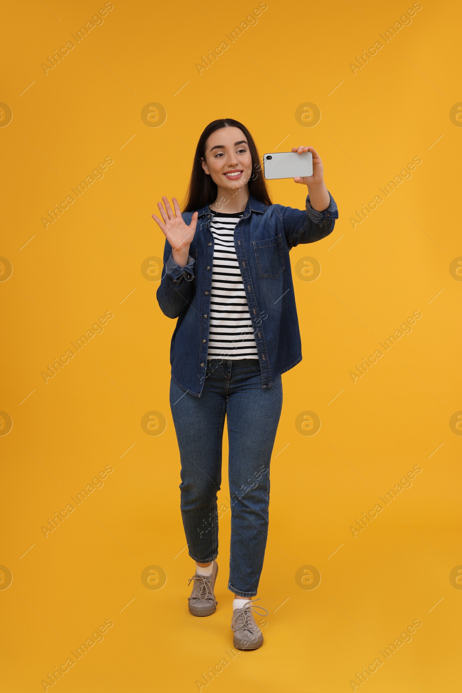 Photo of Smiling young woman taking selfie with smartphone on yellow background