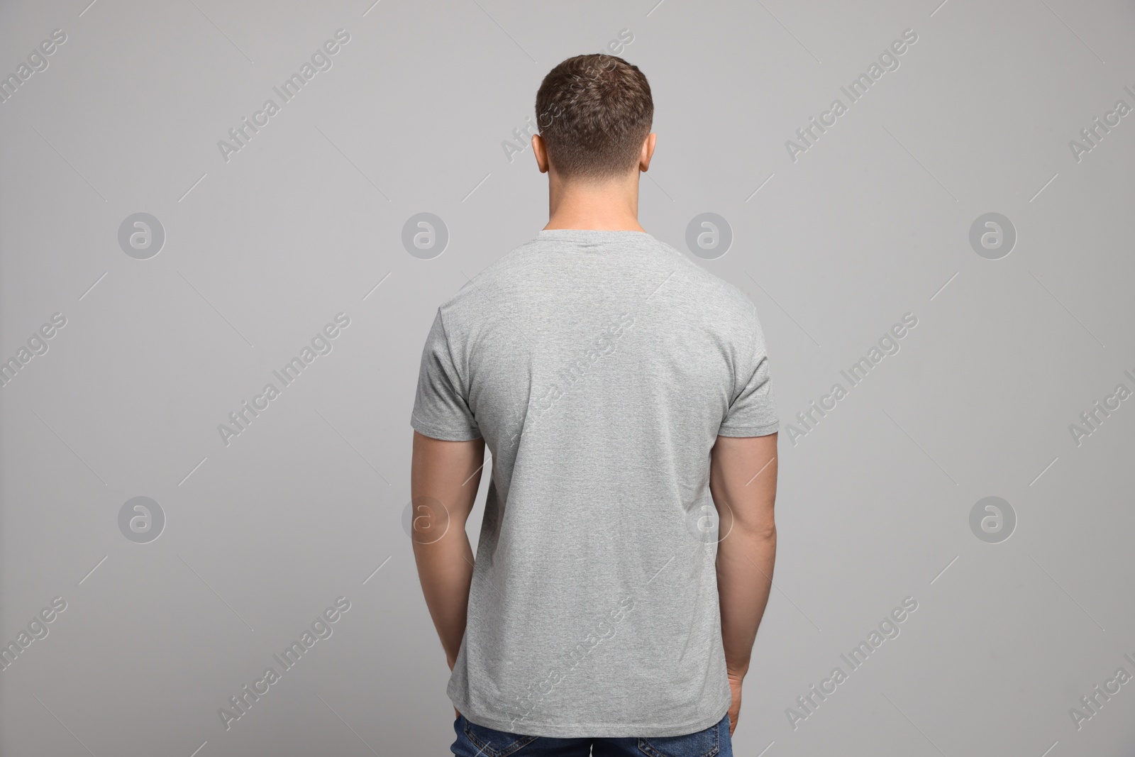 Photo of Man wearing blank t-shirt on light grey background, back view. Mockup for design