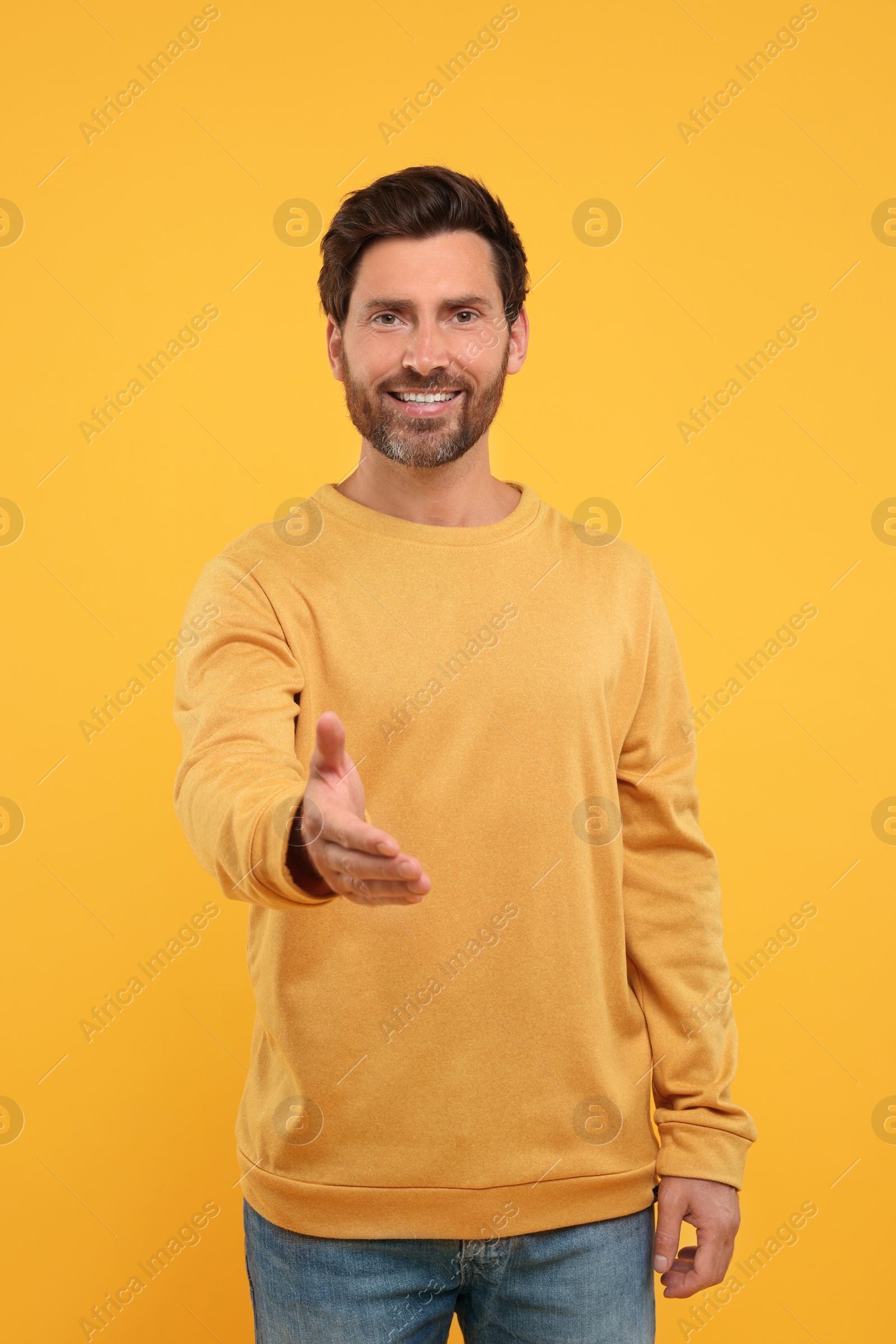 Photo of Happy man welcoming and offering handshake on orange background