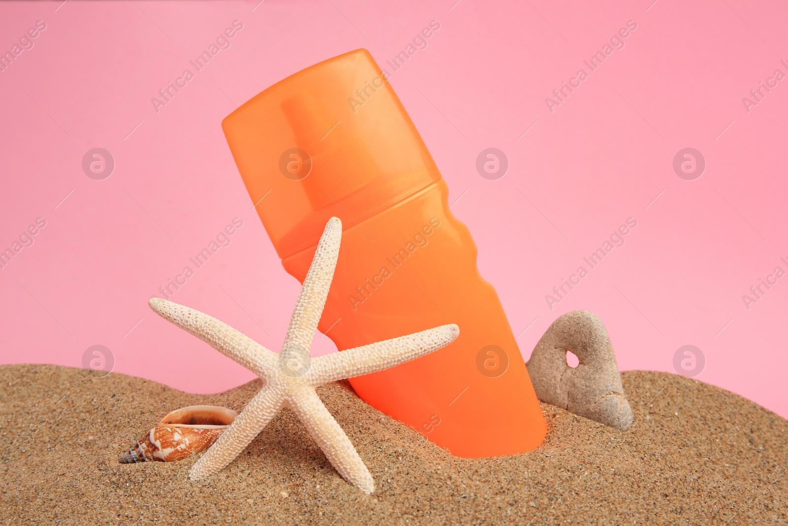 Photo of Sand with sunscreen, starfish, stone and seashell against pink background. Sun protection care